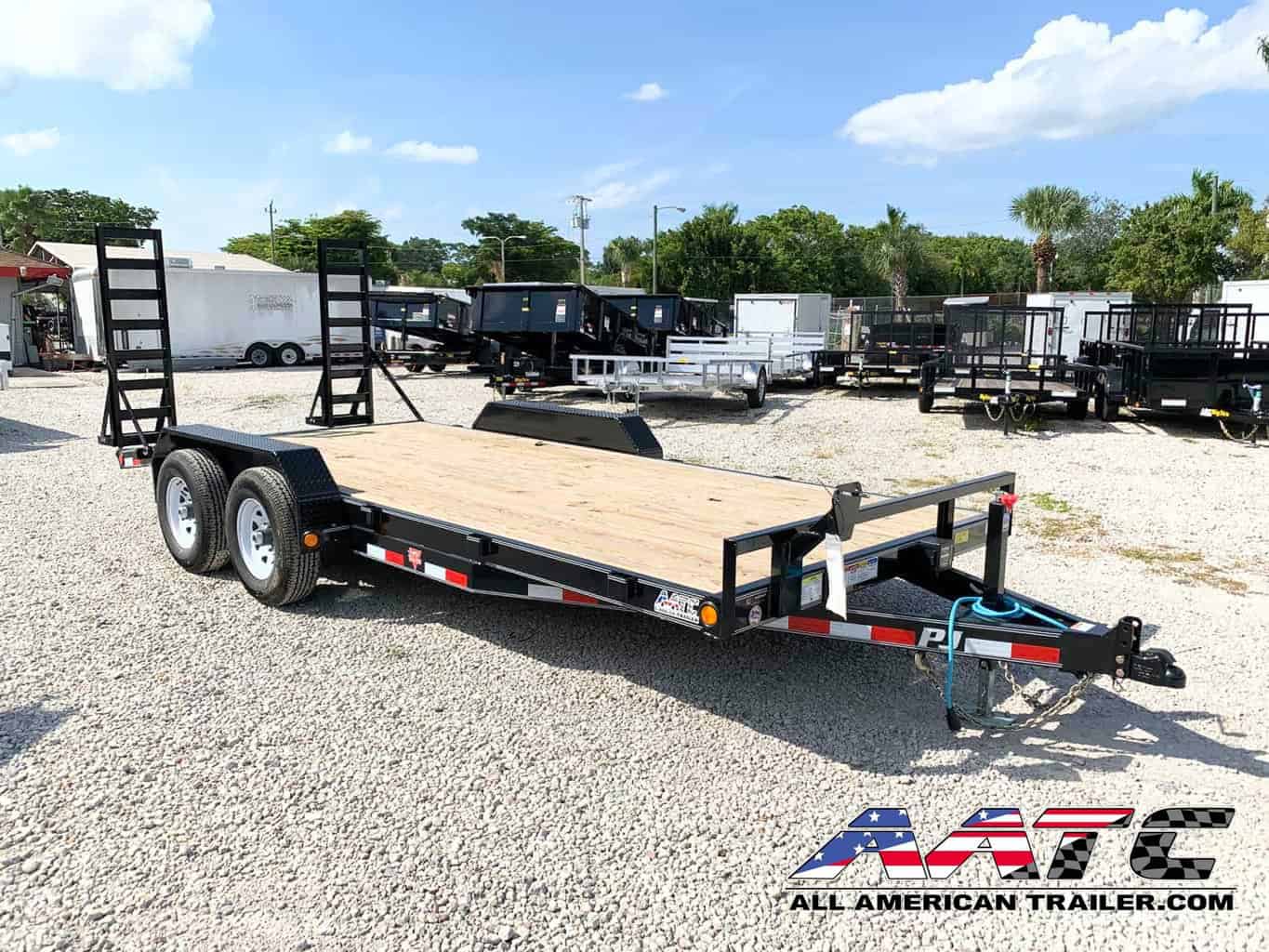 A black PJ 18-foot equipment trailer with a 10,000 GVWR. This PJ Trailer features a straight deck with fold-up ramps, providing a load capacity of 7060 lbs. It is designed for bumper pull hitch type towing and equipped with electric brakes for added safety. The trailer is perfect for hauling various equipment and cargo, and it's from the renowned PJ Trailers brand.
