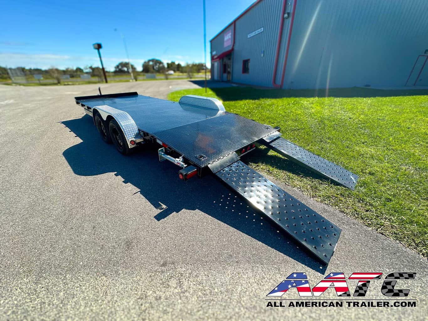 A PJ 20-foot steel deck car hauler trailer, model CH-202-SIR, designed for efficient vehicle transportation. This PJ Trailer features a 4-foot dovetail with 5-foot slide-in ramps, making it easy to load and unload vehicles. With a 3.5-ton capacity, a 7,000 GVWR, electric brakes, and a black finish, it's a durable and practical choice for car hauling. The bumper pull design allows for convenient towing.
